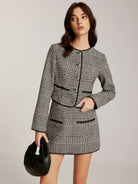 Hahnentritt-Zweiteiler mit Blazer und Minirock, ergänzt durch eleganten weißen Rollkragenpullover und schwarze Accessoires.