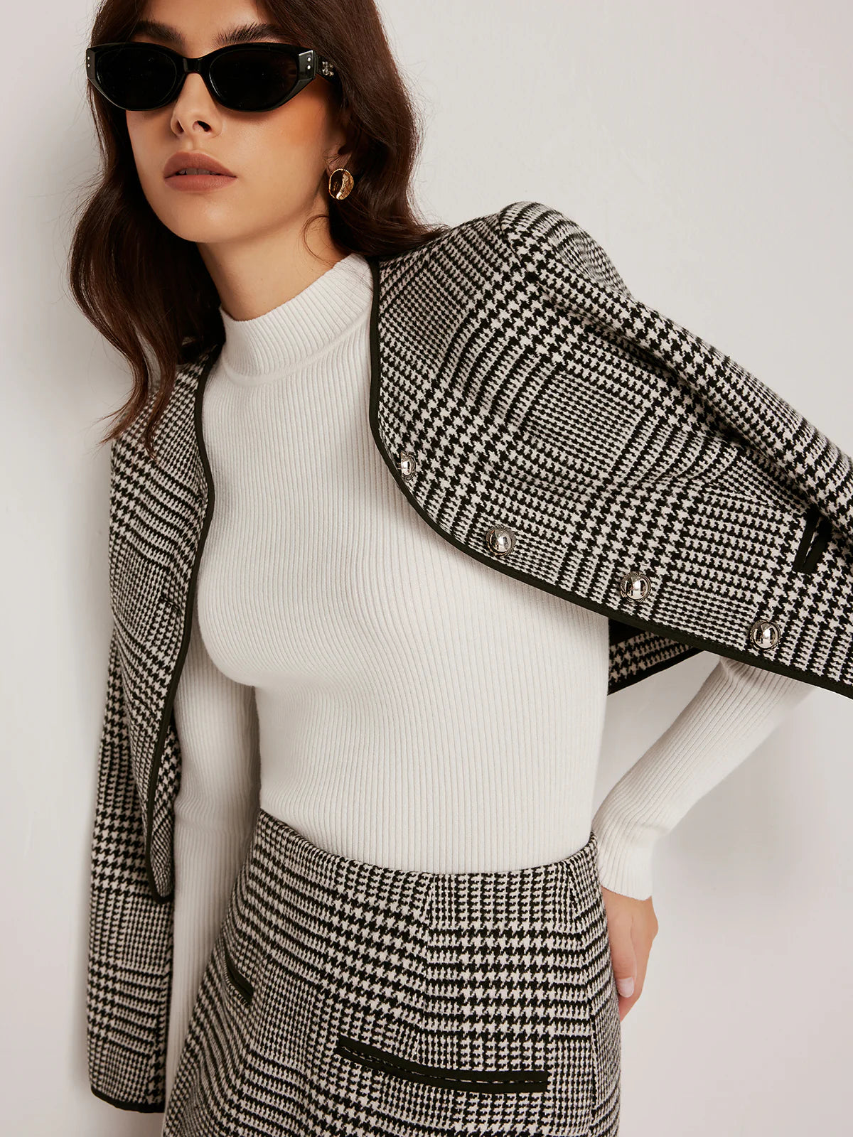 Hahnentritt-Zweiteiler mit Blazer und Minirock, ergänzt durch eleganten weißen Rollkragenpullover und schwarze Accessoires.