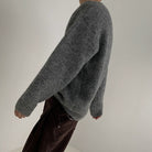 Seitenansicht eines grauen Pullovers, getragen von einem Modell mit lässigem Look.