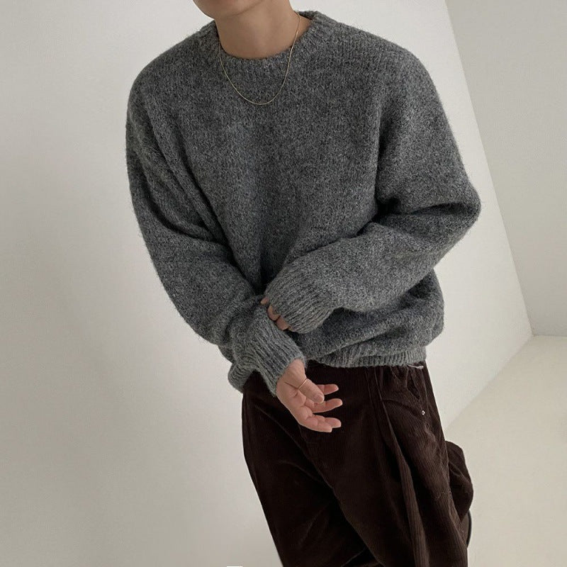 Modell trägt einen grauen Pullover mit lockerer Passform und langen Ärmeln, kombiniert mit braunen Hosen.