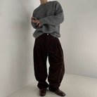 Vollansicht eines Modells in einem grauen Pullover und braunen Hosen, aufgenommen in einem minimalistischen Raum.
