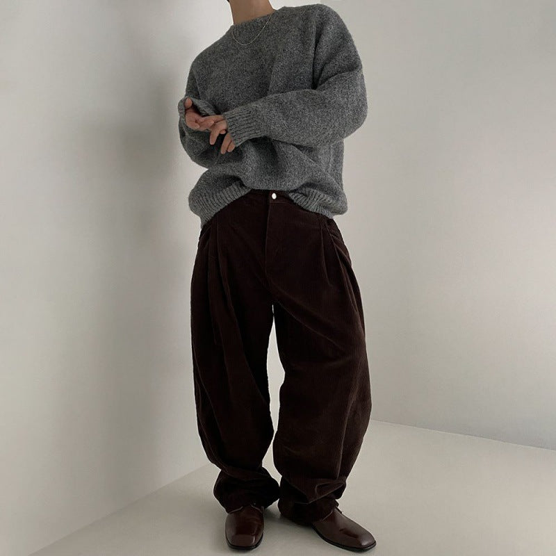 Vollansicht eines Modells in einem grauen Pullover und braunen Hosen, aufgenommen in einem minimalistischen Raum.
