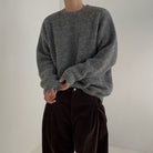 Detailaufnahme eines Modells im grauen Pullover mit leicht aufgekrempelten Ärmeln, betont die weiche Textur des Stoffes.
