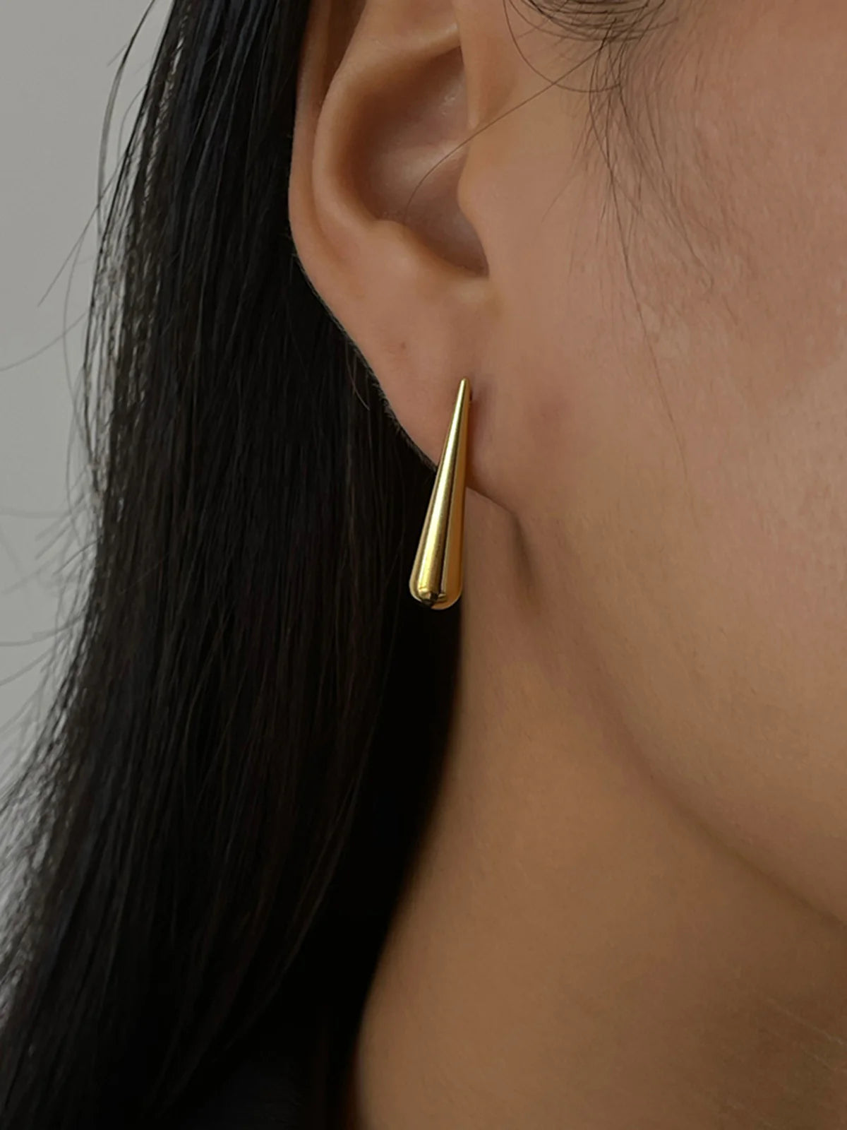 Ein-Paar-schlank-silber-gold-tropfenförmige-Ohrringe-an-einem-Ohr.