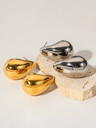 Ein-Paar-goldene-und-silberne-Tropfenförmige-Ohrstecker-auf-einem-Dekosteinelement.